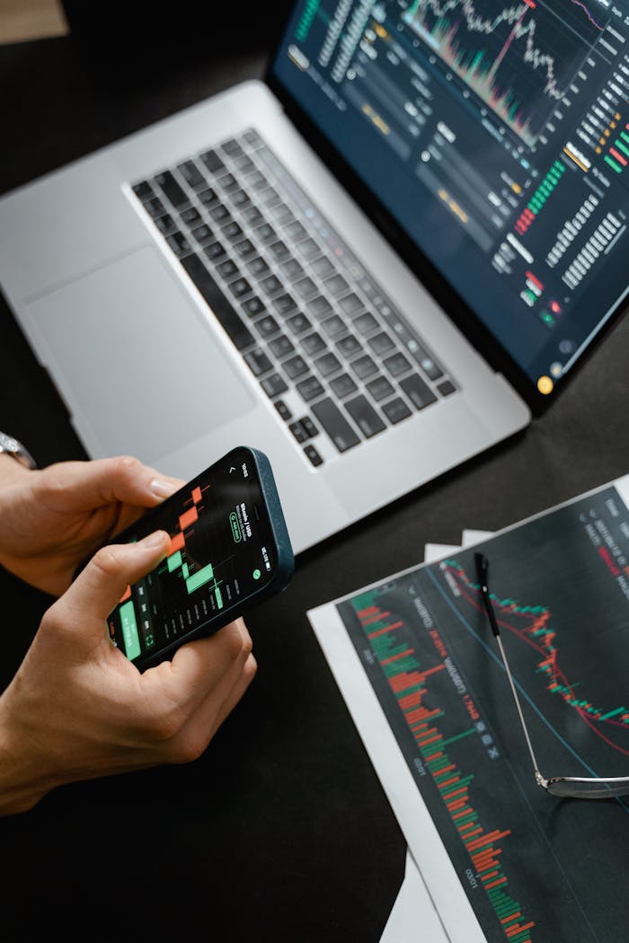 our-services-2 Hands holding phone with financial graph, laptop in view.